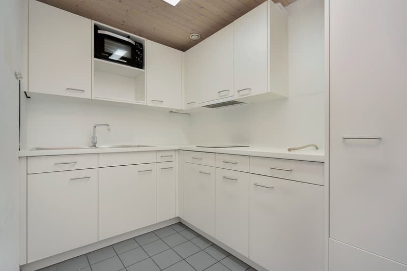 Compact kitchen with white cabinets, built-in microwave, and tiled floor.