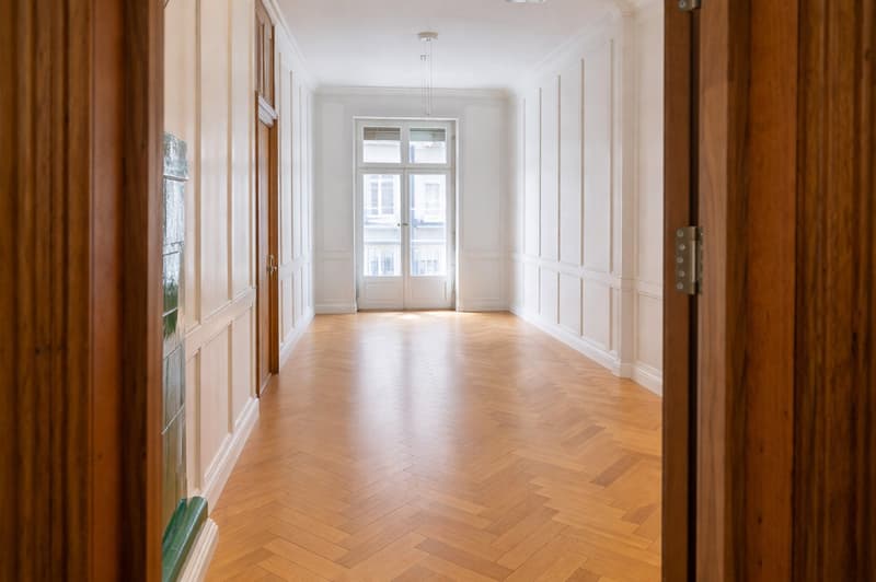 wide hallway with herringbone wooden floor, glass window with balcony, wooden doors