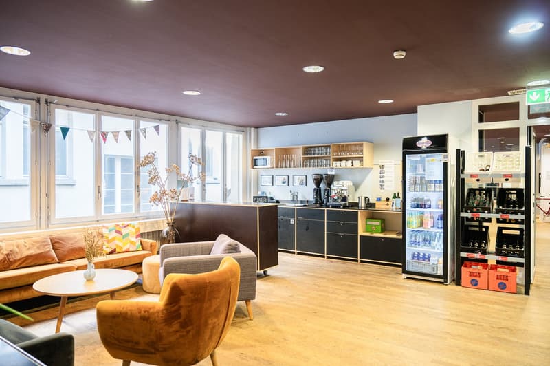 lounge with sofa, armchair, coffee table, wooden floor, window, refrigerator, cabinets, microwave, picture frames, and coffee machine