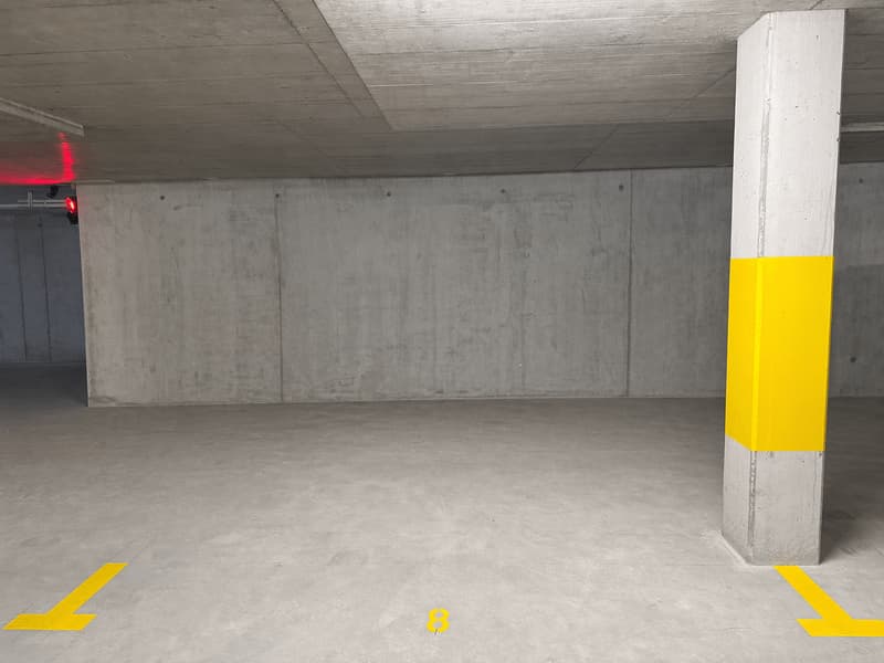 Empty parking area with concrete walls, yellow markings, and a red light