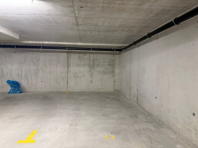 Empty parking space with concrete walls, floor, and ceiling, yellow markings, and a blue plastic bag