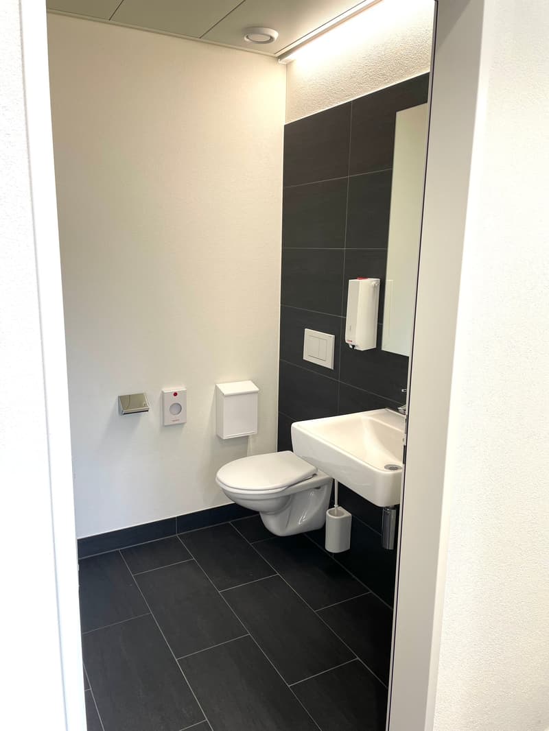 Bathroom with white toilet, sink, and black tiled floor