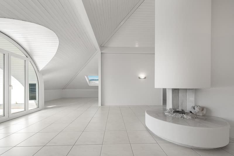 Spacious attic room with white walls and ceiling, large windows, and a modern fireplace feature