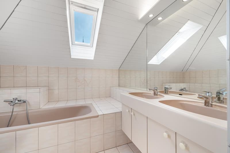 Spacious bathroom with tiled walls, a bathtub, double vanity sinks, and a skylight window providing natural light.
