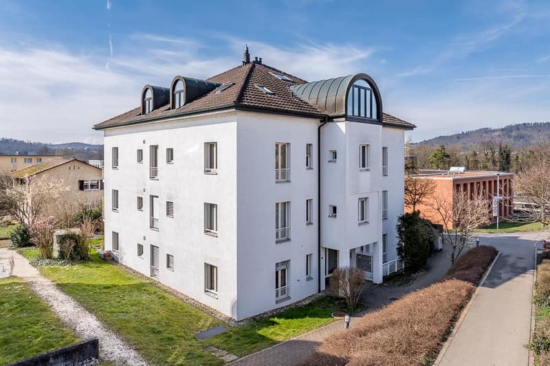 5-story white apartment building with arched windows, tiled roof, and landscaped grounds