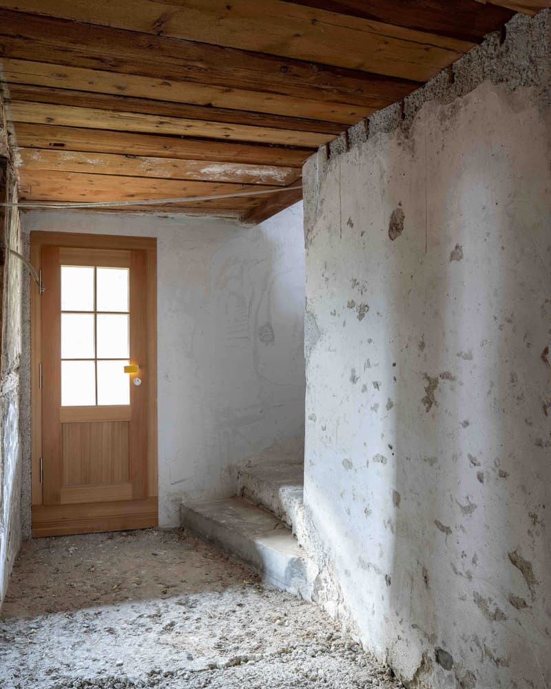Interior of a building, wooden door, stone staircase, rough concrete walls, wooden ceiling beams, unfurnished