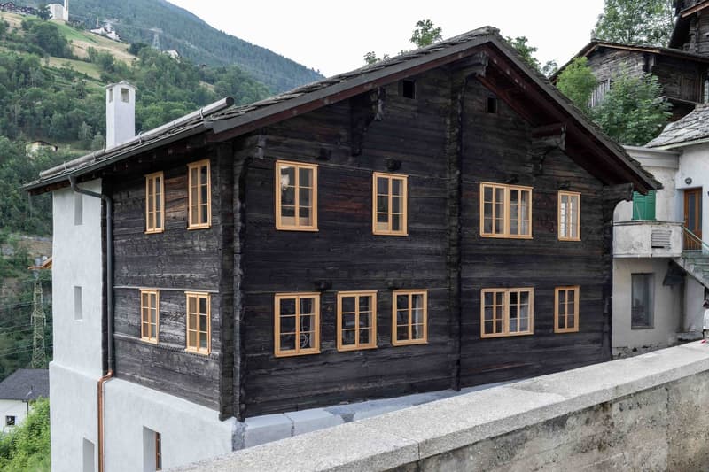 Wooden facade, multiple windows, two stories, chimney, mountains in the background