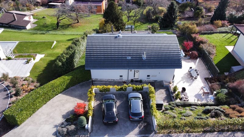 white house, gray roof, two cars parked in front, garden, patio with table and chairs