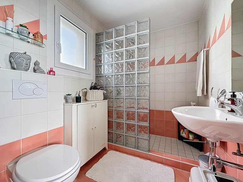 modern bathroom with white and pink tiles, glass block wall, white sink, white toilet, white cabinet, white rug, window