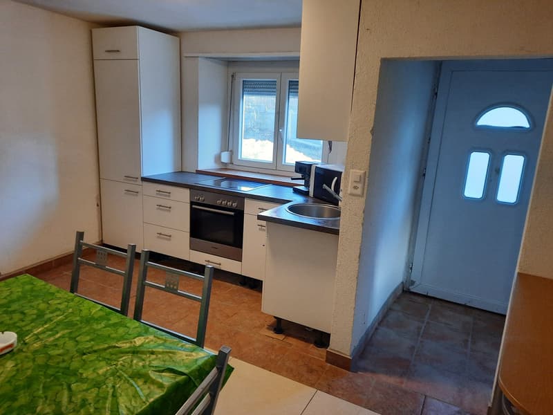 Fully equipped kitchen with white cabinets, stove, oven, and dishwasher. Tile flooring and a window overlooking the exterior. Dining area with a table and chairs.