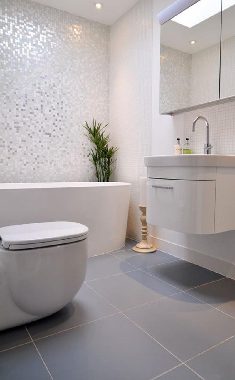 Modern bathroom with white walls, gray tile floor, freestanding bathtub, vanity with sink, and a dishwasher visible.