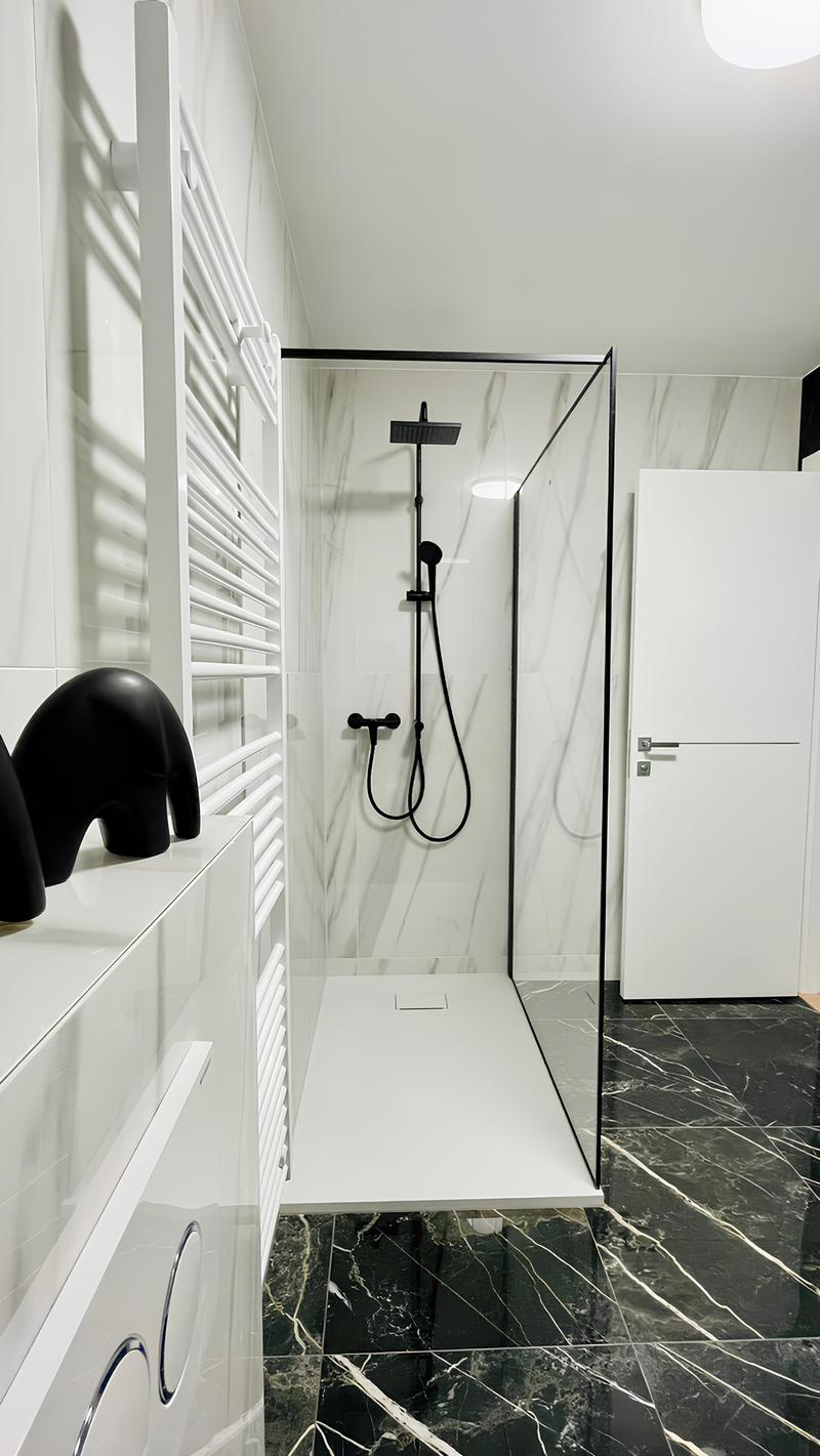 Modern bathroom with white walls, black and white marble floor tiles, a glass shower enclosure, and a black shower fixture.
