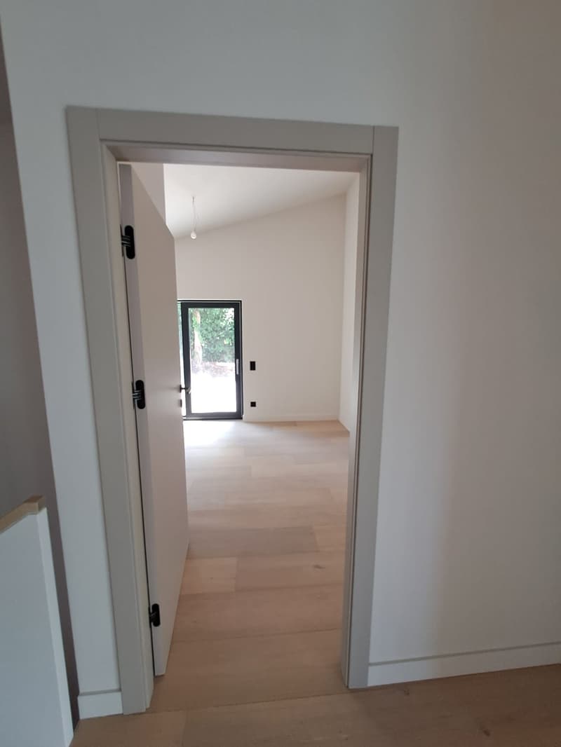Open door to hallway with wooden floor and white walls, sliding door at the end, hanging light