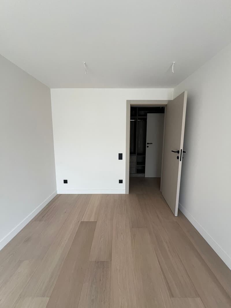 an empty room with wooden flooring, white walls, an open door, a closet