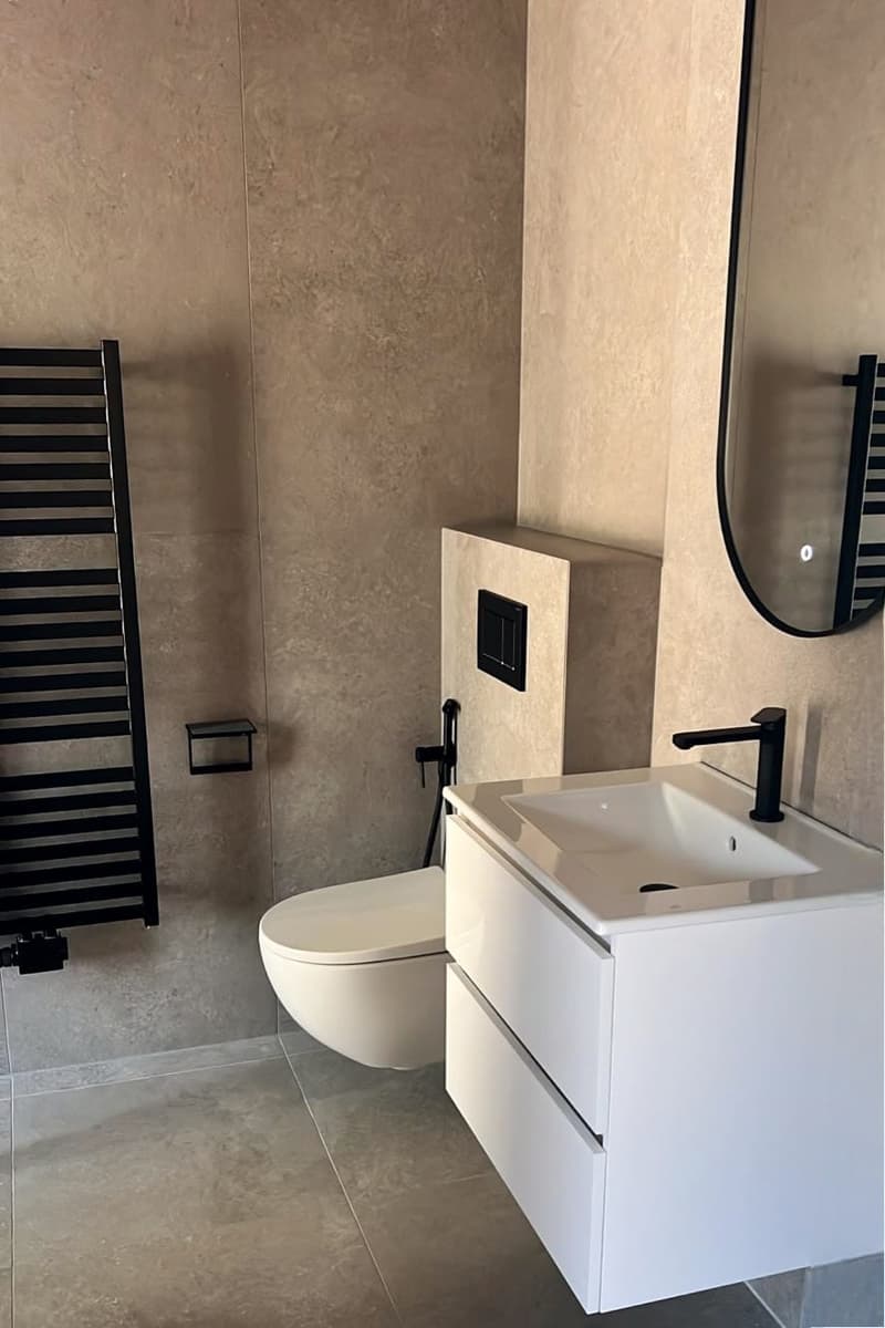 modern bathroom with white sink, black faucet, white floor and walls, white toilet, black radiator