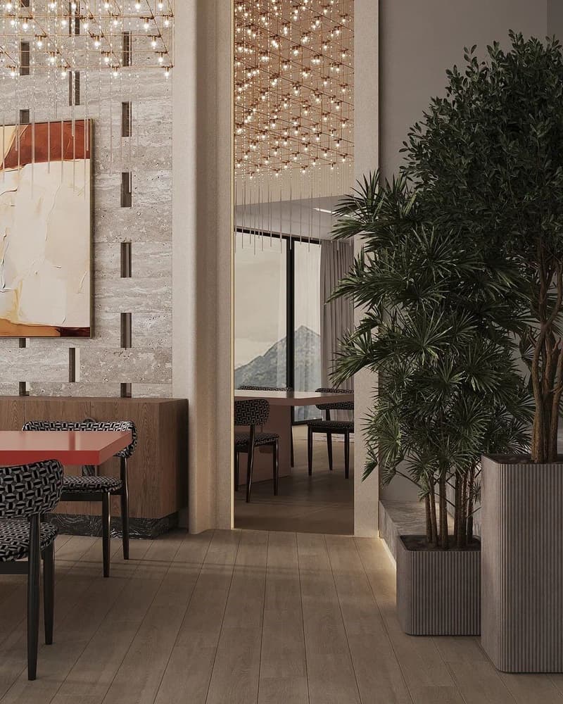 The image shows a modern and stylish dining area with a large window overlooking a balcony or terrace. The space features a stone wall, a chandelier with numerous hanging lights, and potted plants. There is a wooden table with patterned chairs, as well as