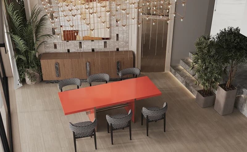 Dining room with a large orange table and six patterned chairs. The room has a mirrored wall with string lights, and there are potted plants in the background.