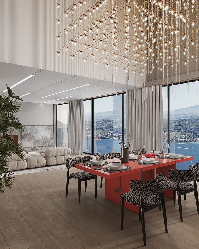Spacious open-plan living and dining area with floor-to-ceiling windows offering a panoramic view of the surrounding landscape. The room features a modern, minimalist design with a large, plush sofa and a sleek, red dining table with black patterned chair