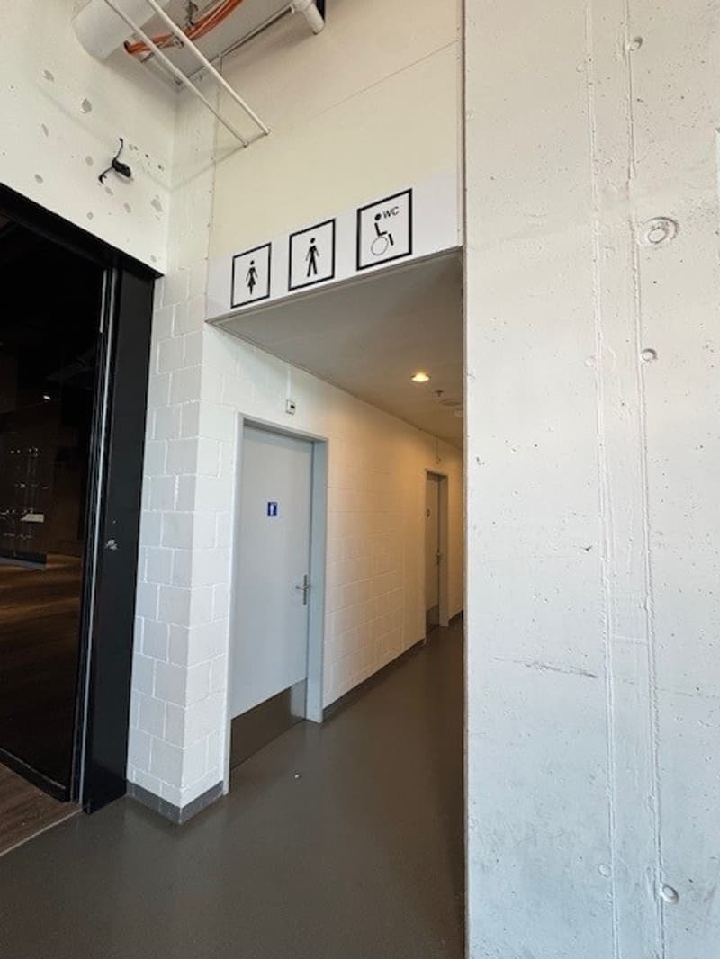 White brick walls, wooden floor, two doors, three signs above the doors