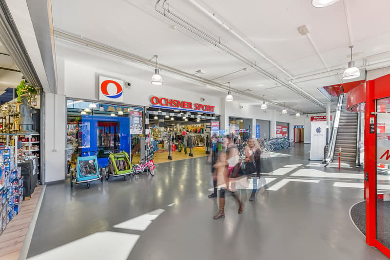 Mall interior, rows of stores, shoppers, escalators, bicycles parked, advertisement banners