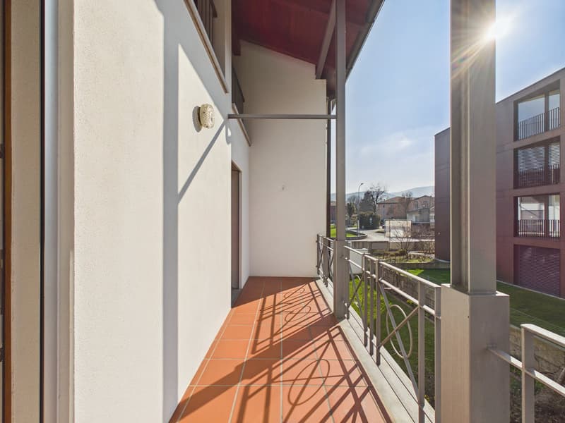 Balcony with red tiles, metal railings, view on grass and a building
