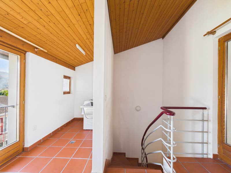 Room with wooden ceiling, white walls, red tiled floor, washing machine, spiral staircase