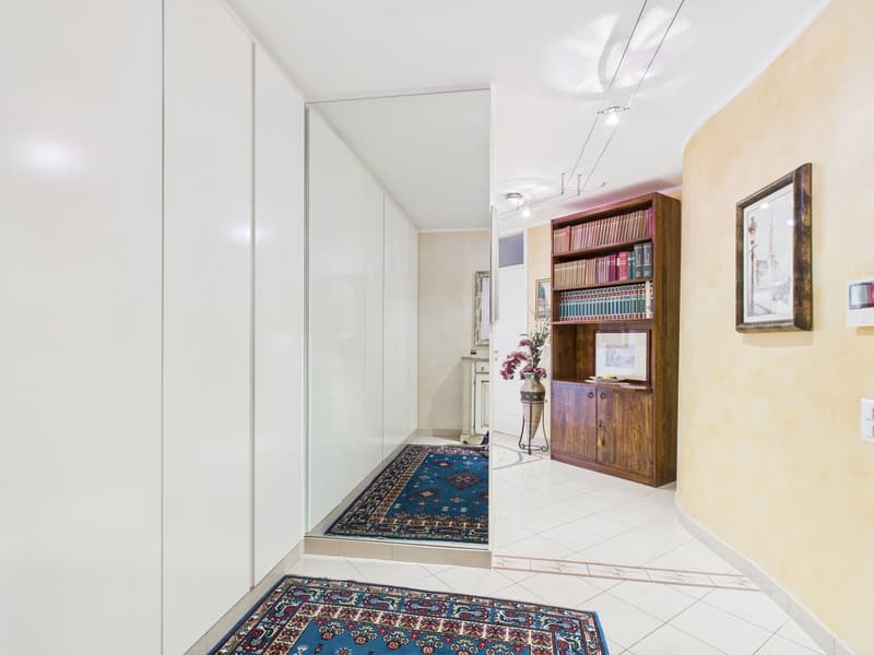 white walls, white tile floor, wooden bookshelf, rug, picture frame, flower vase, mirror