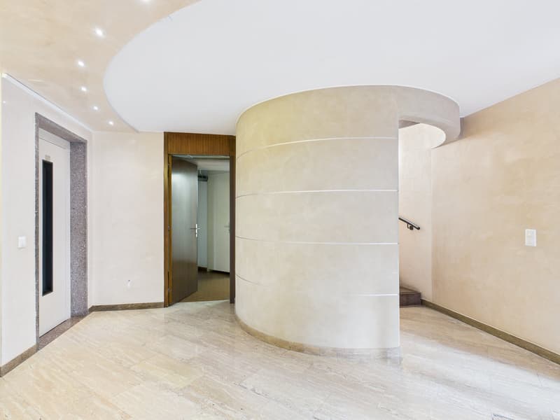 Empty room with a large curved wall, wooden door, tiled floor, and a staircase