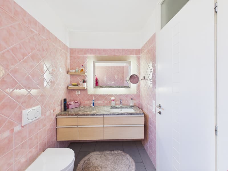 Bathroom with pink tiles, wooden cabinet, marble countertop, sink, mirror, and toilet