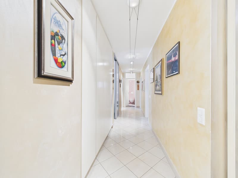 White tiled floor, beige walls, framed pictures, ceiling lights