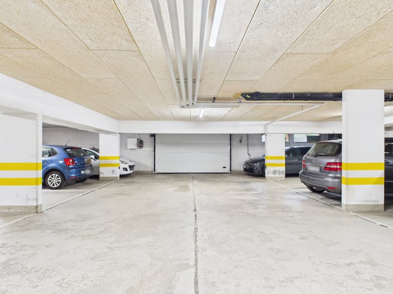 underground parking lot with 4 cars parked, white and yellow pillars, white ceiling, white walls
