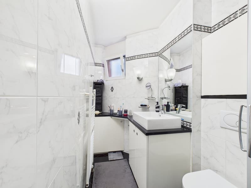 modern bathroom with white marble tiles, white sink, black countertop, white cabinets, mirror, toilet, shower area
