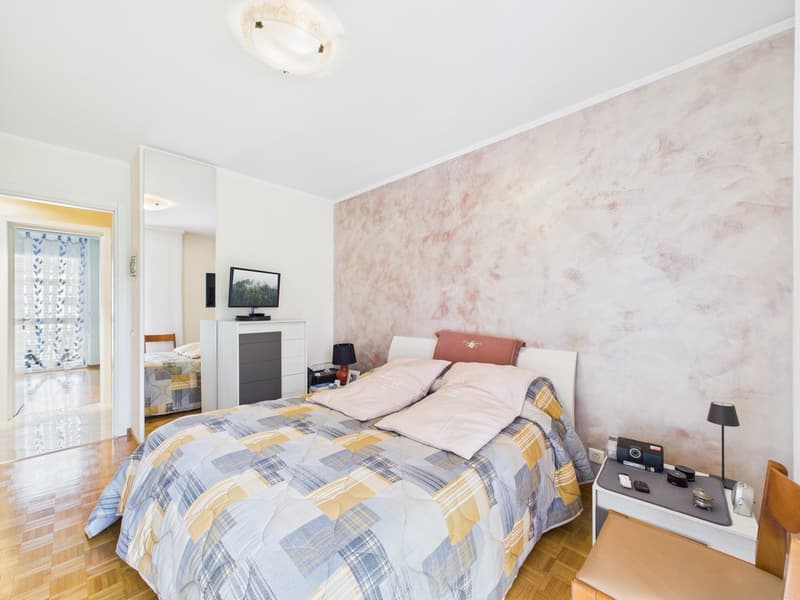 Bedroom with bed, nightstands, lamp, TV, cabinet, mirror, wooden floor, patterned wall