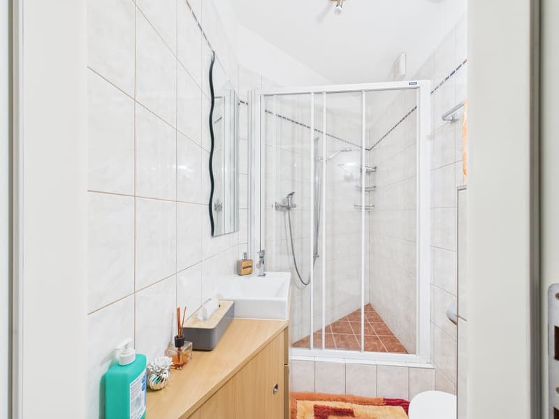 white tiled walls, white sink, glass shower enclosure, mirror, wooden cabinet, toilet