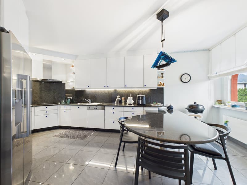 modern kitchen with white cabinets, granite countertops, stainless steel appliances, large dining table, black chairs, hanging lamp, clock, and a window with a view