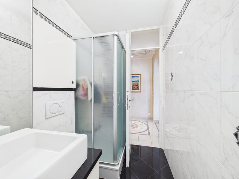 white marble tiles, white sink, glass shower enclosure, black tiled floor, white walls, mirror
