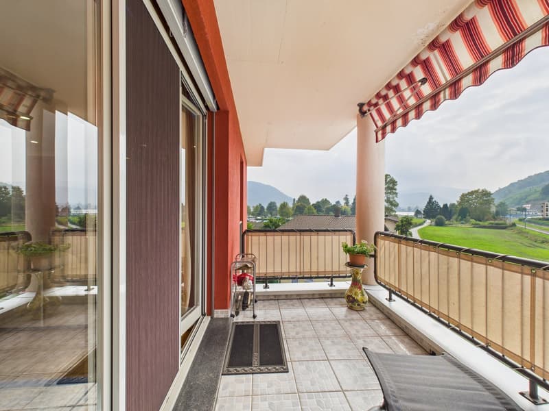 Balcony with tiled floor, metal railing, awning, potted plants, and a view of a grassy field and mountains