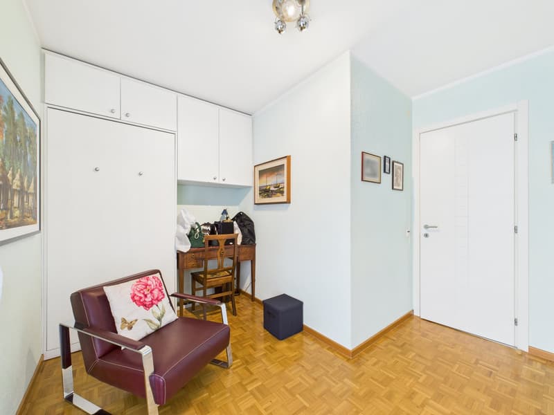 wooden floor, white walls, white cabinets, desk, chair, storage box, picture frames, lamp