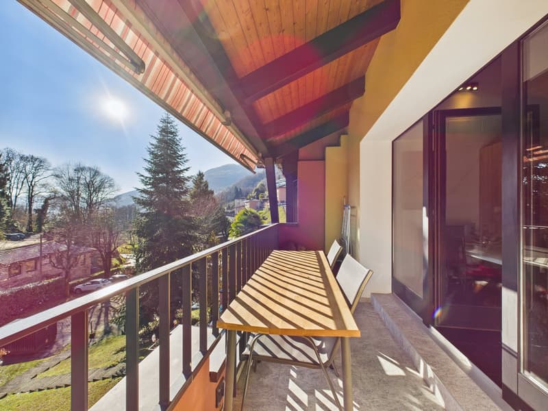 Balcony with wooden table and chairs, wooden ceiling, glass doors, view of trees and mountains