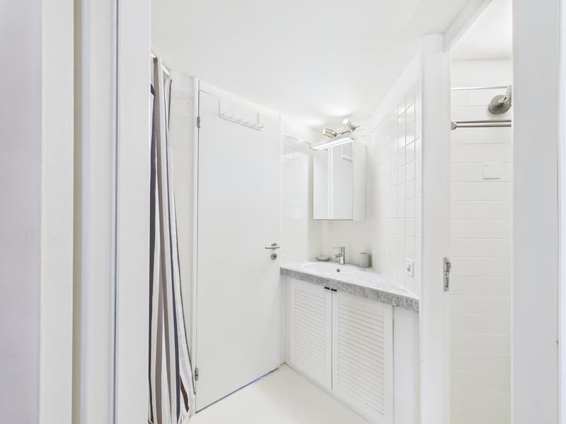 Bathroom with white tiles, white sink, white cabinets, shower area, mirror, and towel rack.