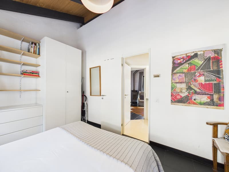 Bedroom with bed, shelves, wardrobe, mirror, open door, painting, wooden chair, and a fireplace