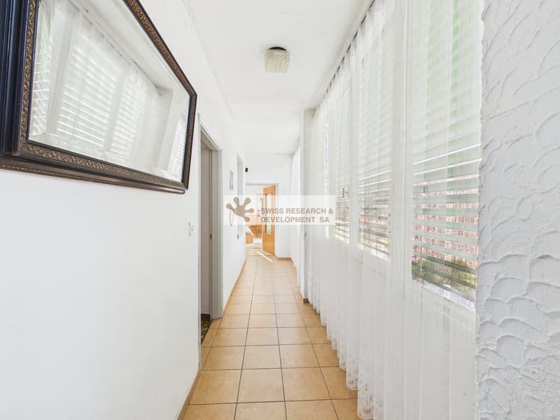 long hallway, white walls, tiled floor, white curtains, mirror on the wall