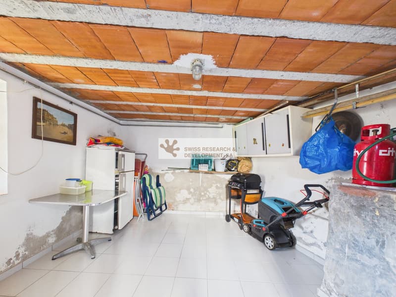 Storage room with tiled floor, wooden ceiling, table, chairs, appliances, and various items