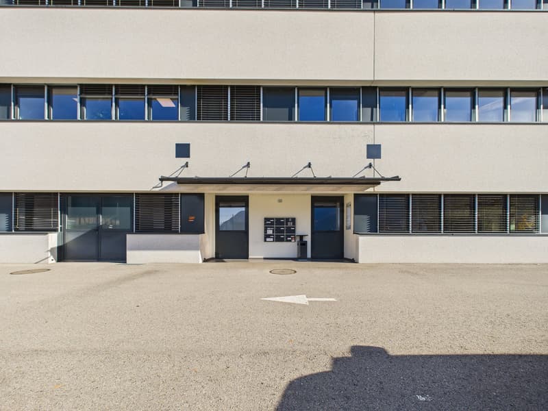 Modern building with multiple windows, two entrances, and a parking area in front