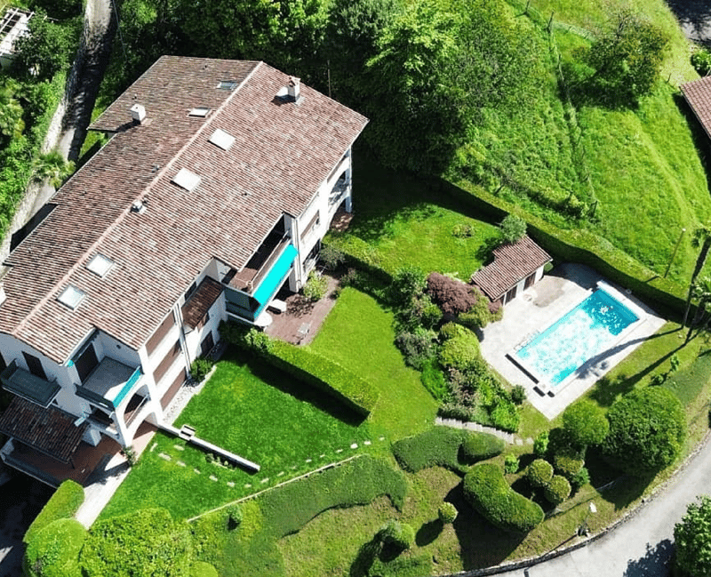 2 story house, brown roof, white walls, swimming pool, garden, green grass, trees