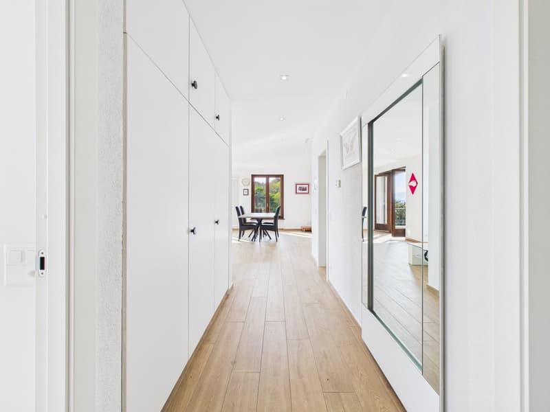 long hallway, wooden floor, white walls, large mirror, dining area with table and chairs