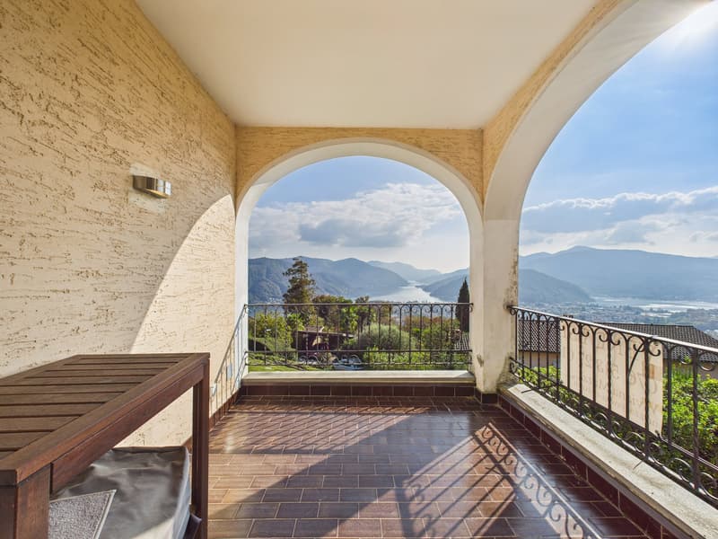 Balcony with tiled floor, black metal railing, wooden table, view of mountains and lake