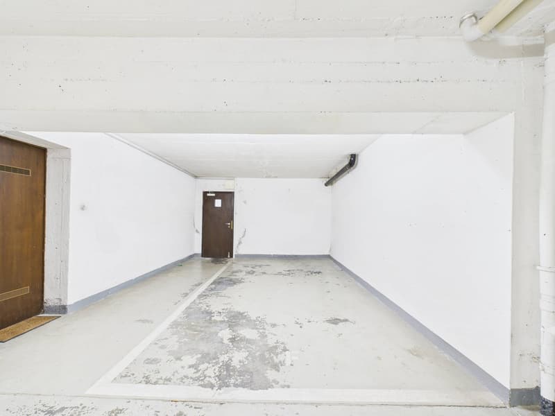 Empty parking space, white walls, wooden doors, concrete floor, pipes on the ceiling