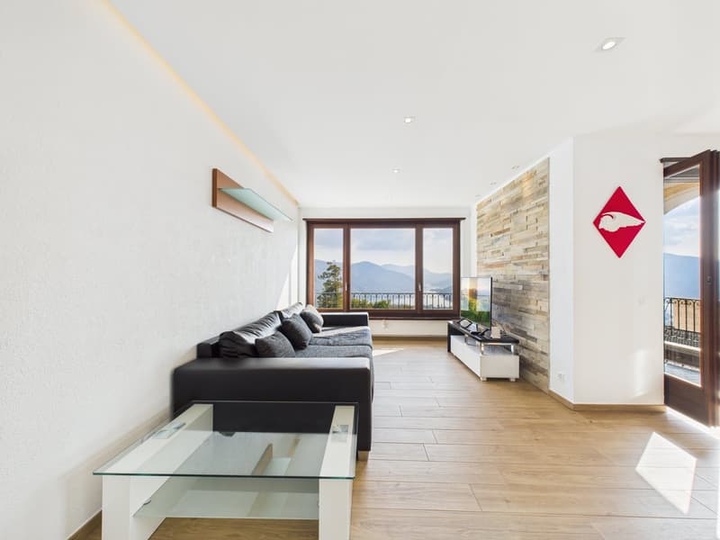 modern living room with black leather sofa, glass coffee table, TV, brick wall, balcony with railings, wooden floor, white walls