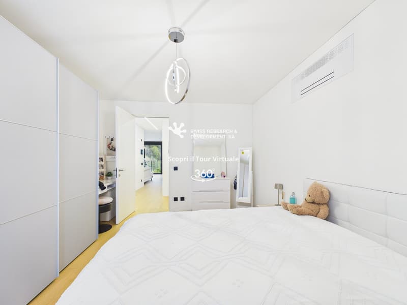 modern bedroom with white walls, wooden floor, large bed, white headboard, white wardrobe, white cabinet, mirror, lamp, teddy bear, and a chandelier
